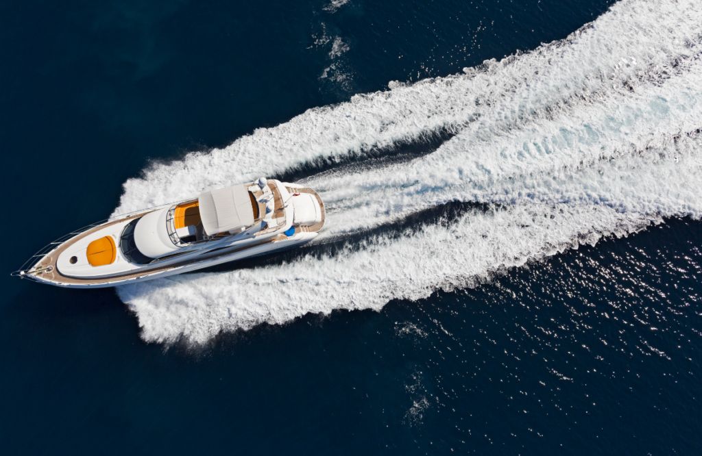 Dark blue deep ocean with a white and orange yacht sailing through the center leaving a trail of white water