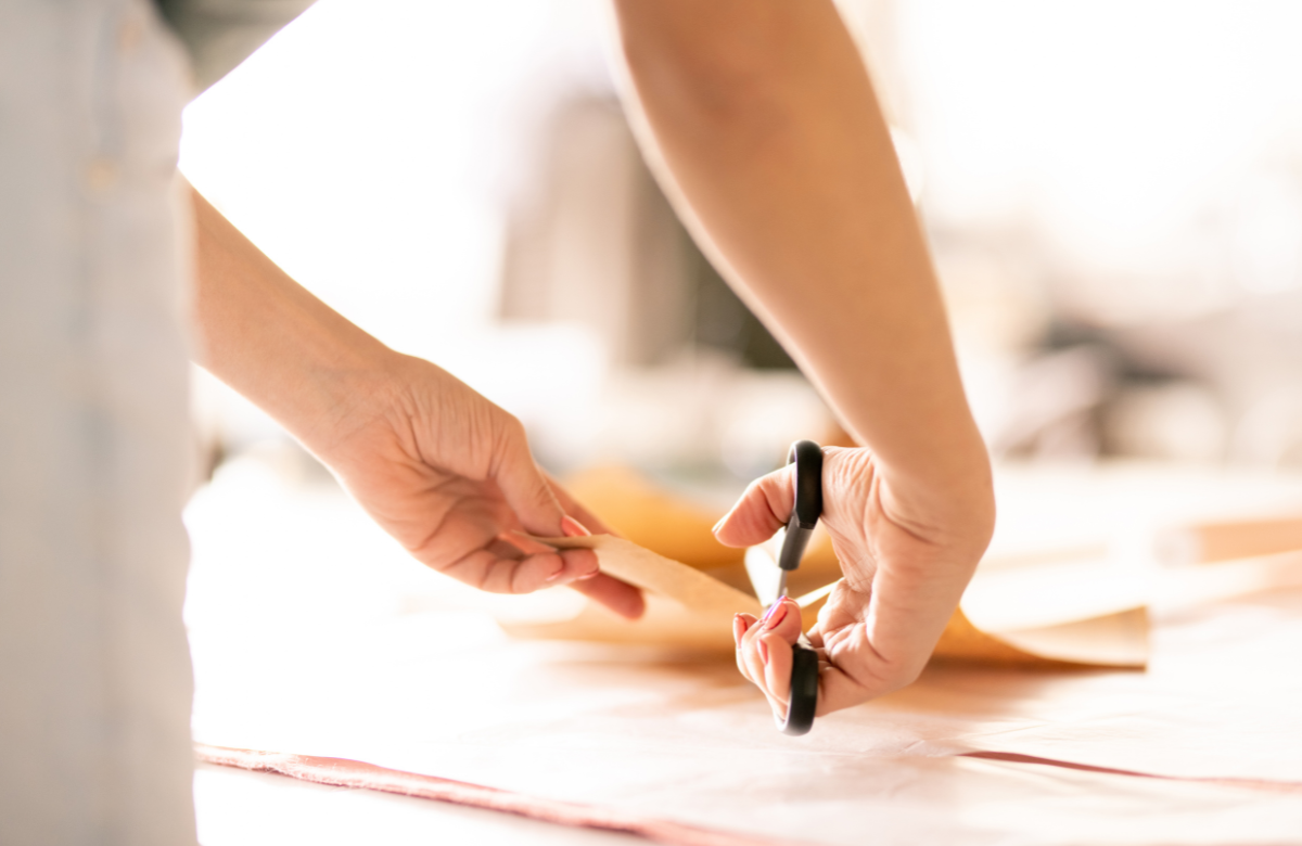 Hands cutting through brown paper using black handled scissors