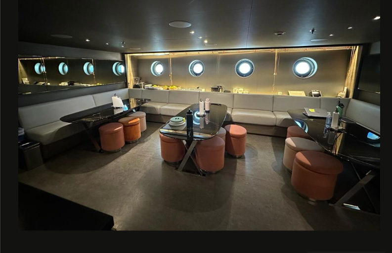 Three tables surrounding by soft cushioned stools with cushion furnishings surrounding the border. Dim candle lit crew quarters.