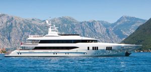 Superyacht on bright blue waters in front of mountain range.
