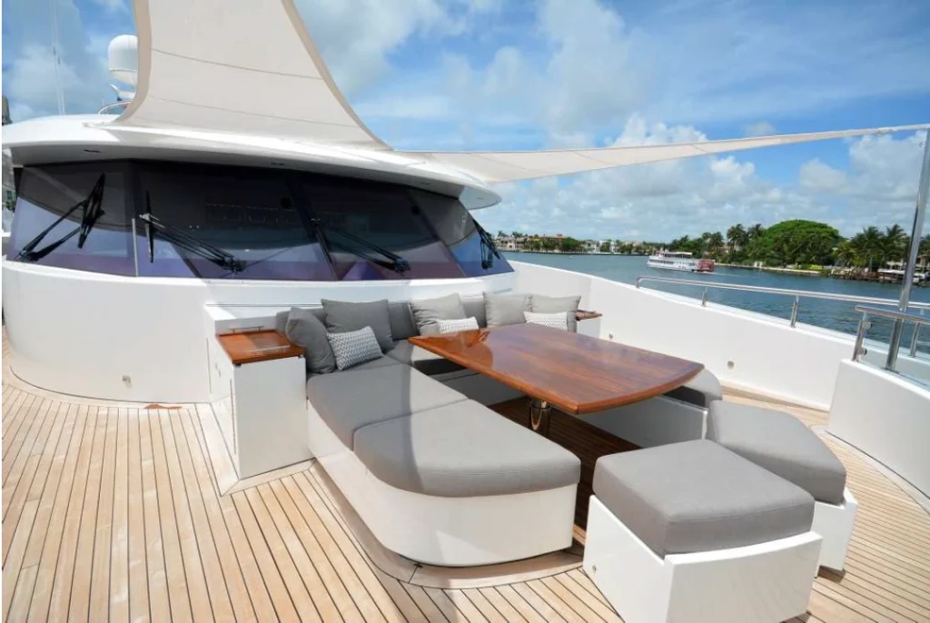 Yacht sail awnings fanned out over grey yacht furnishings and a brown outdoor dining table on the yacht deck.