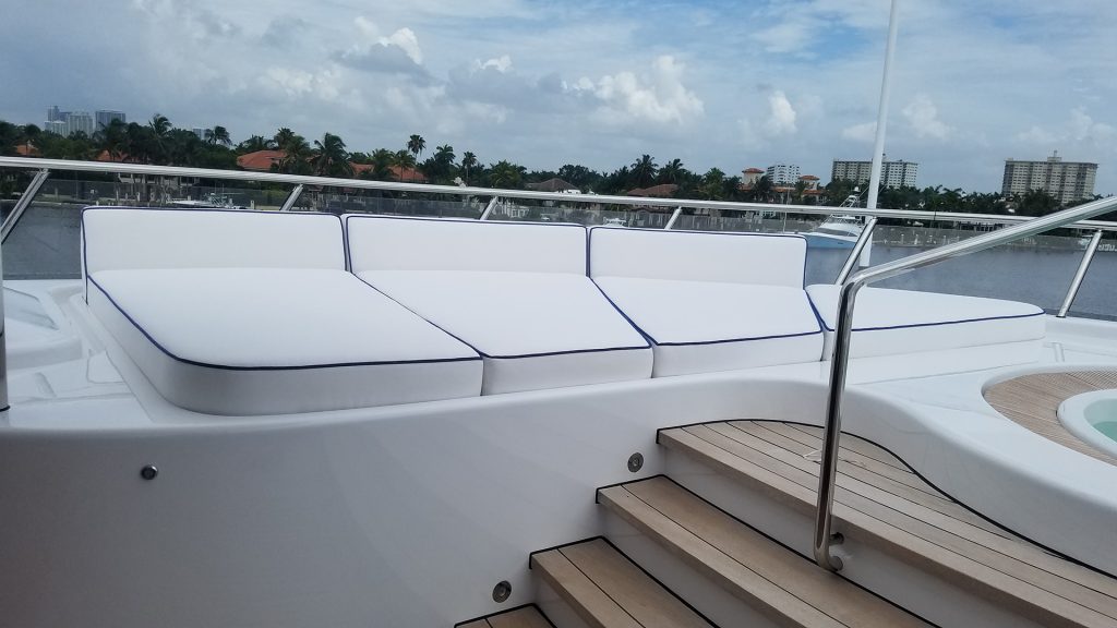 Four white leather cushions as a sunpad beside wooden yacht deck steps and a jacuzzi.