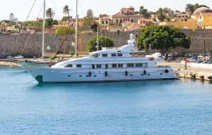 Large Superyacht on clear water next to shore.