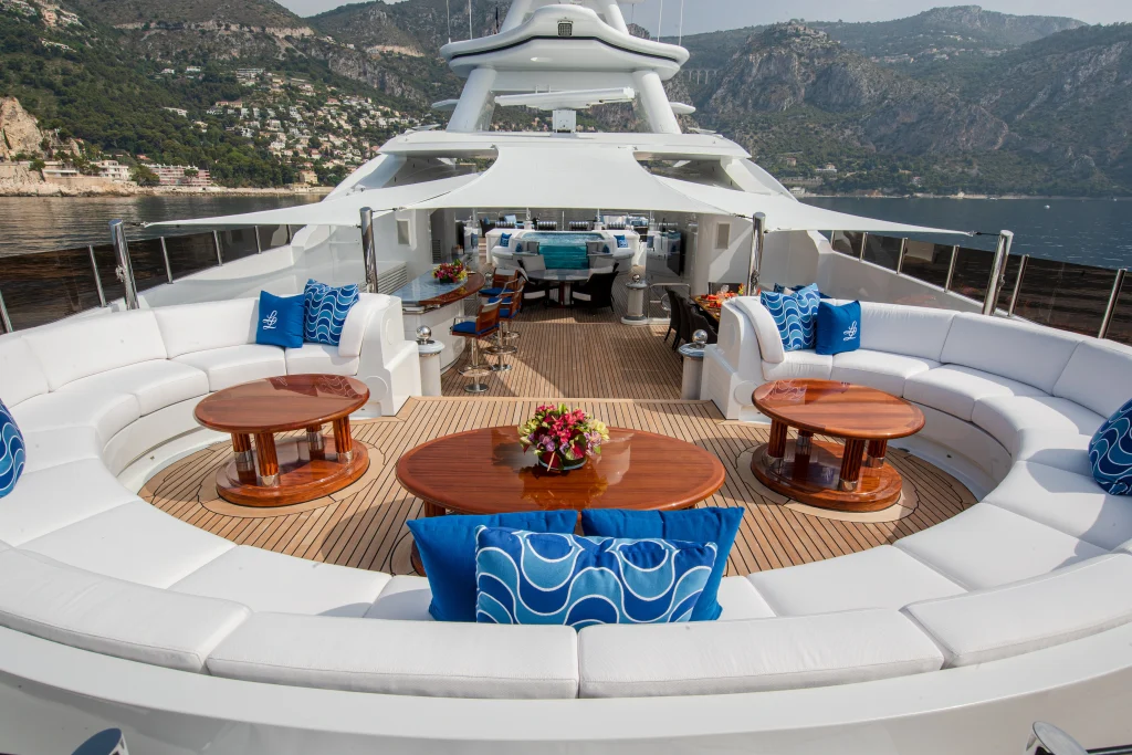 Yacht white cushions and sofas on a yacht deck with tables, with white sun awning above. A jacuzzi is in the background on deck..